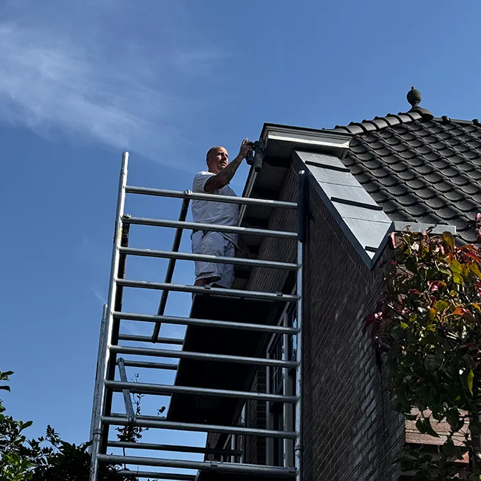Schilder op een steiger bij de dakgoot van een woning
